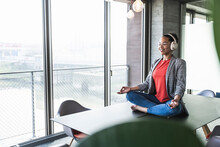 Businesswoman Listening Music And Meditating At Work Place