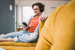 © Westend61 - Cheerful man listening music through wireless headphones using smart phone in living room