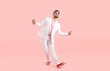 © Studio Romantic - Happy funny guy in white suit dancing isolated on pastel pink background. Full body shot of cheerful goofy carefree man in modern suit, sneakers and glasses dancing and having fun in the studio