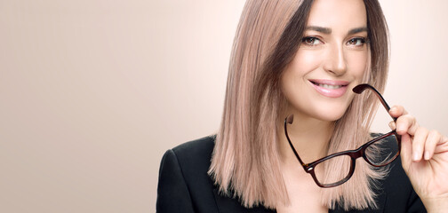 Successful businesswoman with glasses. Stylish modern woman with pinkish blonde hair and eyewear smiling at camera over beige background