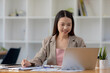 © kamiphotos - A beautiful Asian businesswoman sitting in her private office, she is checking company financial documents, she is a female executive of a startup company. Concept of financial management.