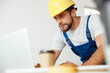 © Kostiantyn - Focused handyman in uniform and hard hat using laptop while starting renovation work indoors