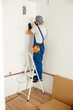 © Kostiantyn - Electrician, handyman standing on a ladder while working on installing socket on wall at home