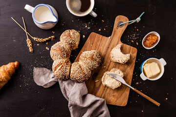 Eating continental breakfast - gold bread roll (bagel) with sesame, butter, jam and coffee