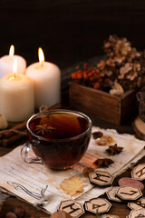 wooden runes are lying on the table among the papers with notes. there is a mug of tea next to it. a
