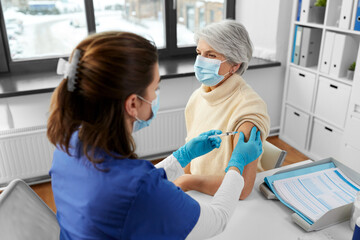 Sticker - medicine, health and vaccination concept - doctor or nurse with syringe making vaccine or drug injection to senior woman in mask at hospital