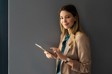 Wall Mural - Attractive young businesswoman using a digital tablet while standing in front of windows in office