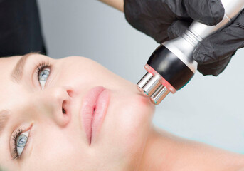 A young woman is lying on the RF-lifting procedure for face skin tightening and face contour correction. Close-up.