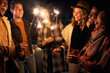 © StratfordProductions - Multi-racial group of friends lighting sparklers at a party on a rooftop terrace. Nightlife in the city.