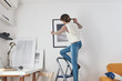 © astrosystem - Girl child teenager on the ladder hanging pictures and photos on the shelf and wall at home.