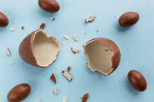 Two halves of a broken chocolate egg for children with small eggs around on a blue background. Copy space in the middle. Easter card, top view