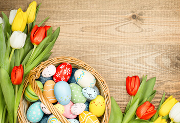  wicker basket with easter eggs and spring tulips on a wooden table top view