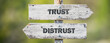 opposite signs on wooden signpost with the text quote trust distrust engraved. Web banner format.