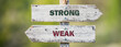 opposite signs on wooden signpost with the text quote strong weak engraved. Web banner format.