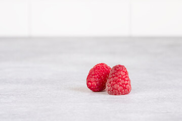 Two raspberries on a gray table. Red fresh raspberries on gray background