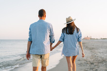 Rear View Of Young Happy Couple Two Friends Family Man Woman In Blue Shirt Clothes Hold Hands Walk Stroll Together At Sunrise Sea Beach Ocean Outdoor Exotic Shore On Summer Day