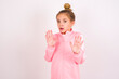 © Roquillo - caucasian little kid girl with bun hairstyle wearing pink tracksuit over white background Moving away hands palms showing refusal and denial with afraid and disgusting expression. Stop and forbidden.