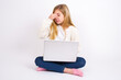 © Jihan - Very upset, caucasian teen girl sitting with laptop in lotus position on white background touching nose between closed eyes, wants to cry, having stressful relationship or having troubles with work