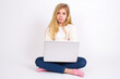 © Jihan - caucasian teen girl sitting with laptop in lotus position on white background bitting his mouth and looking worried and scared crossing arms, worry and doubt.