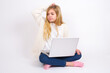© Jihan - caucasian teen girl sitting with laptop in lotus position on white background saying: Oops, what did I do? Holding hand on head with frightened and regret expression.