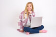 © Jihan - Carefree successful  caucasian teen girl sitting with laptop in lotus position on white background touching jawline gazing camera tilting head grinning white teeth delighted. Dental care concept.