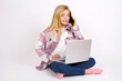© Jihan - Portrait of successful joyful  caucasian teen girl sitting with laptop in lotus position on white background talking on mobile phone with friend. Lifestyle and communication concept