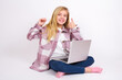 © Jihan - caucasian teen girl sitting with laptop in lotus position on white background holding an invisible braces aligner and rising thumb up, recommending this new treatment. Dental healthcare concept.