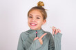© Roquillo - little caucasian kid girl with hair bun wearing technical shirt over white background holding an invisible aligner and pointing at it. Dental healthcare and confidence concept.