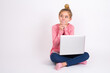 © Jihan - Curious caucasian teen girl sitting with laptop in lotus position on white background keeps hands under chin bites lips and looks with interest aside.