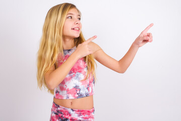 Wall Mural - little caucasian kid girl wearing sport clothing over white background smile excited directing fingers look empty space