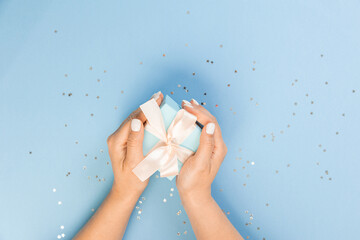 Wall Mural - A hand holds a blue gift box on a blue background with glitter stars. top view, copy space