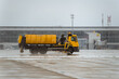 © alexanderon - Yellow aerodrome Maintenance truck spraying De-icing Fluids to prevent runway freezing. Airport in winter. Anti icing runway procedure