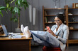 Lazy african american businesswoman procrastinating at workplace sit with feet on desk use smartphone, chat with friend or scroll social media. Entrepreneur female in formalwear rest with mobile phone