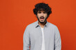 Shocked surprised stupefied displeased sullen amazed young bearded Indian man 20s years old wears blue shirt looking camera keeping mouth wide open isolated on plain orange background studio portrait.
