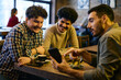 © Drazen - Cheerful male friends look at something funny on cell phone in cafe.