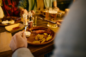 Close-up of man eats sausage during lunch with his friends in pub.