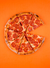 Wall Mural - whole, cooked and sliced peperoni pizza on a bright orange background