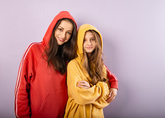 Wall Mural - Happy smiling beautiful young mother and cute daughter posing in fashion trendy yellow and red hoodie together on purple studio background with empty copy space. Happy loving