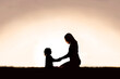 Mother Sitting Holding Hands with Young Child Outside at Sunset.