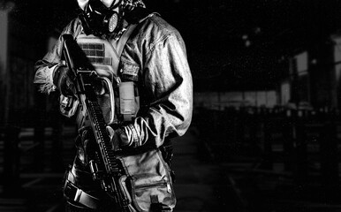 Wall Mural - Black and white photo of urban soldier in tactical military outfit and gas mask standing with rifle and gas mask on dark factory background.