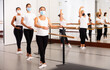 © JackF - Women of different ages in face masks exercising ballet moves in training room.