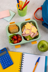 Wall Mural - Healthy school lunch box with sandwich and salad on the workplace near backpack. School supplies, books, apple and a bottle of water