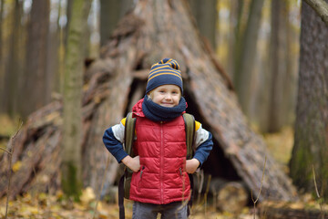 Wall Mural - Little boy scout during hiking in autumn forest. Behind the child is teepee hut. Adventure, scouting and hiking tourism for kids.