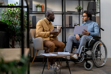 Aufkleber - African-American businessman with drink communicating with his Caucasian colleague in wheelchair at working meeting in urban office
