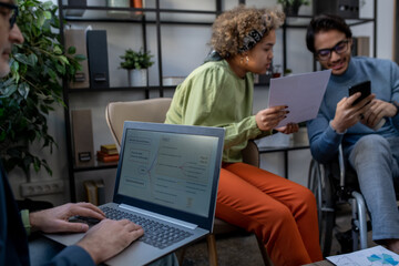 Aufkleber - Mature economist analyzing data on laptop screen against two young intercultural coworkers discussing financial document