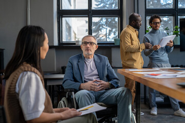 Aufkleber - Mature businessman in wheelchair listening to young female colleague at working meeting while sitting against two intercultural coworkers