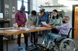 © pressmaster - Mature man in wheelchair and his Asian female colleague discussing document with financial data among group of coworkers
