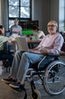 © pressmaster - Mature employee with laptop on his knees sitting in wheelchair in front of camera against group of young intercultural colleagues