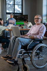 Aufkleber - Mature employee with laptop on his knees sitting in wheelchair in front of camera against group of young intercultural colleagues