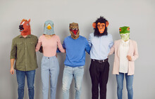Team Of Happy Young People Wearing Funny Crazy Strange Eccentric Carnival Fancy Dress Party Animal Masks Standing Together And Hugging Each Other. Studio Portrait. Teamwork, Fun, Friendship Concepts
